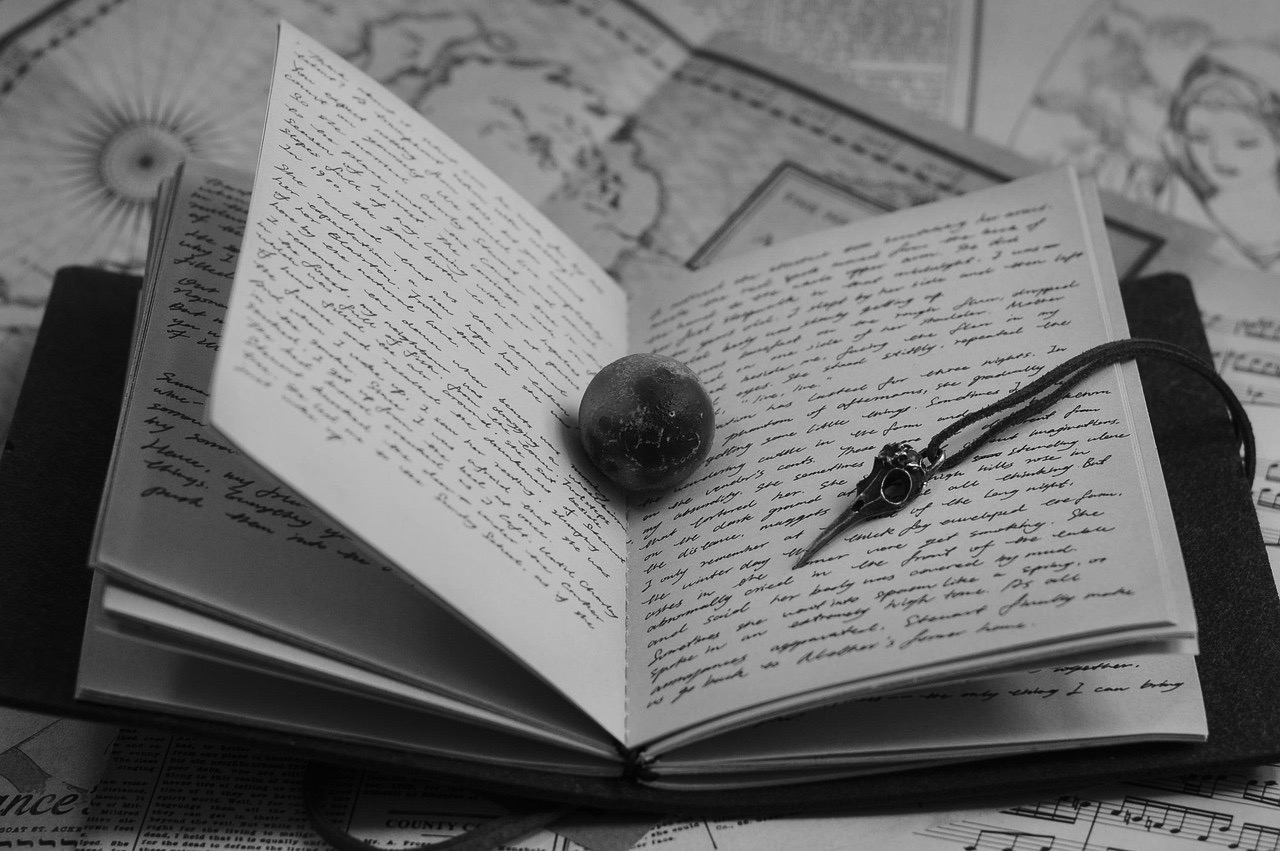 diario scritto a mano aperto con uno strano segnalibro metallico con legaccio e una pallina scura in mezzo alle pagine