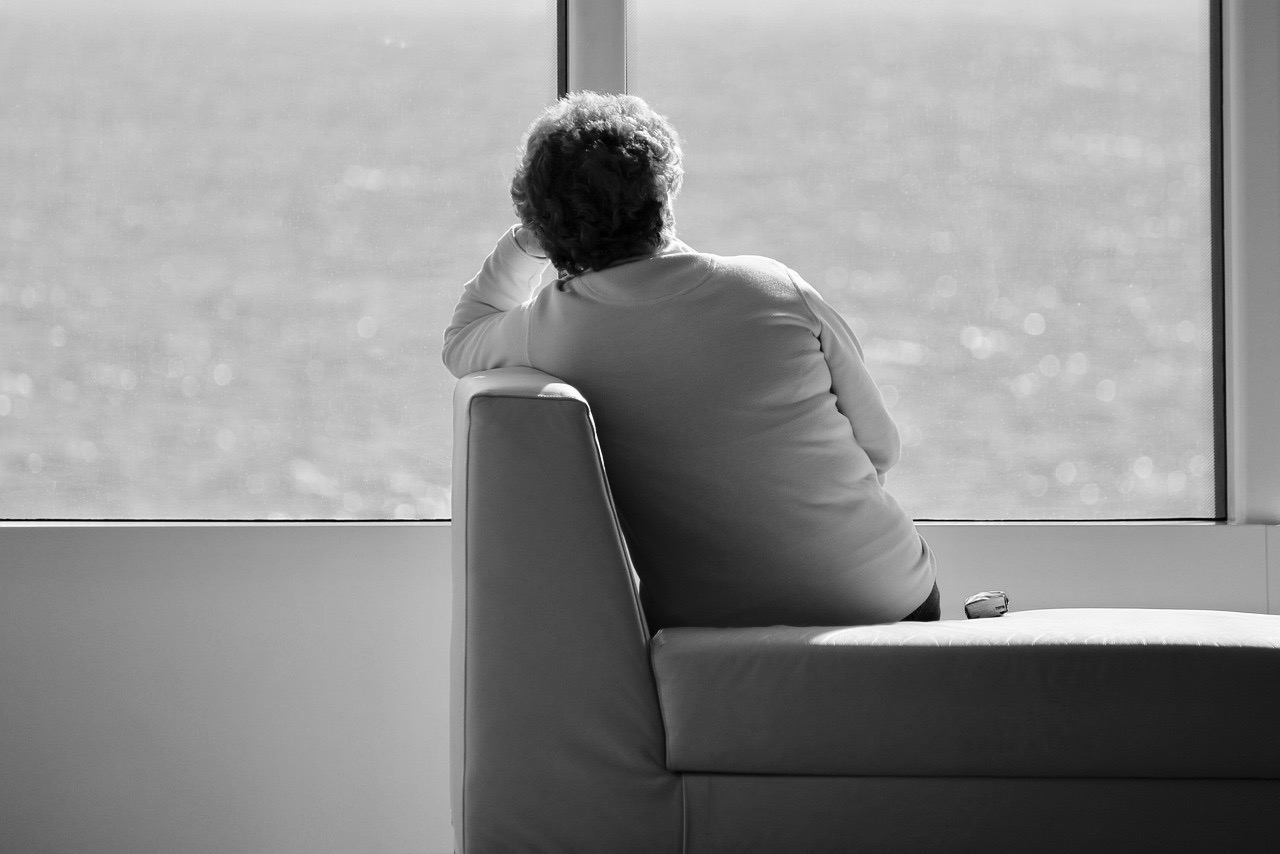 una donna seduta di spalle che osserva dalla finestra il mare