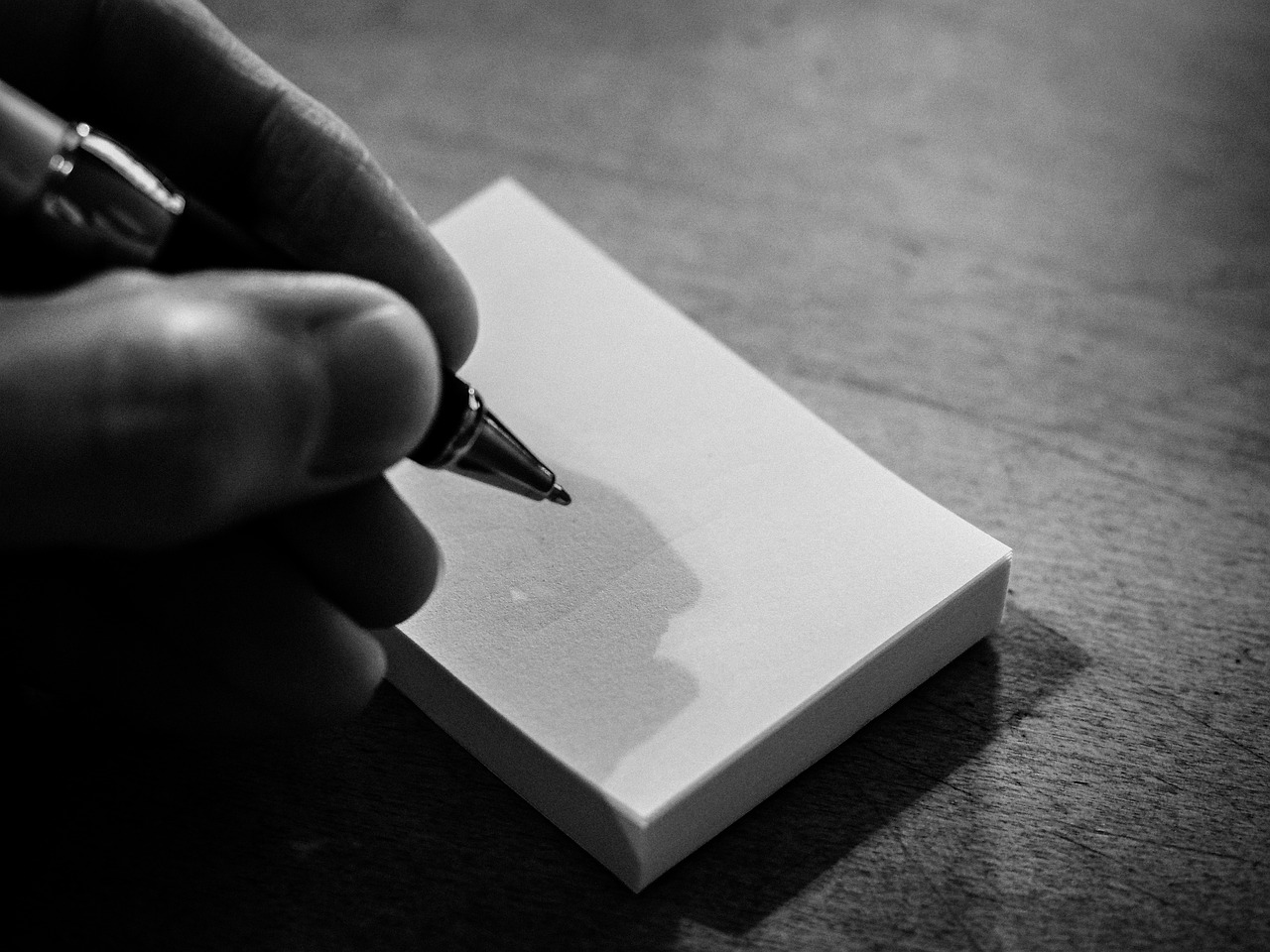 una mano che tiene una penna per scrivere su un minuscolo blocco bianco