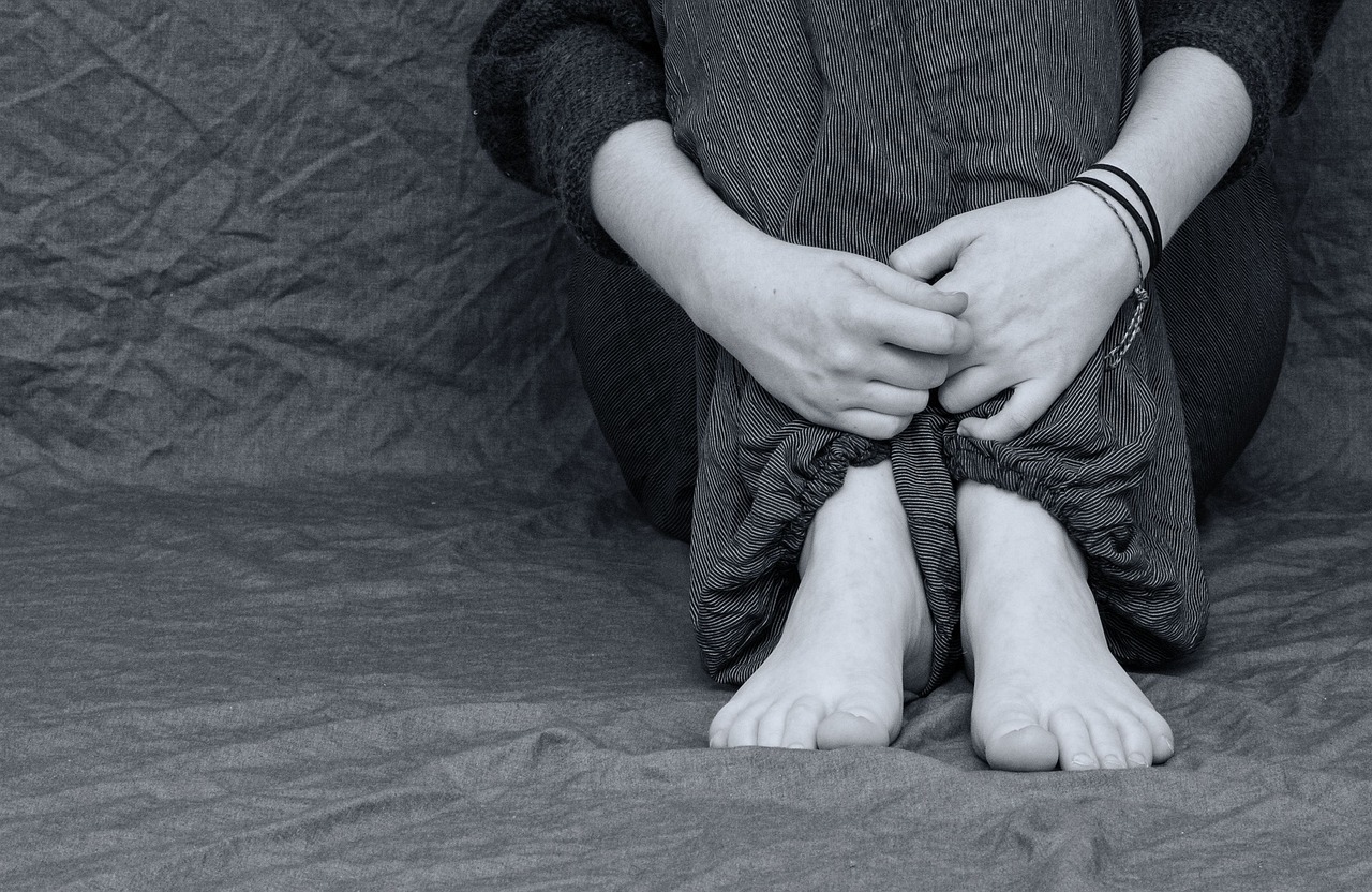 emozioni trattenute primo piano di una ragazza di cui non si vede il volto che abbraccia le proprie gambe da seduta