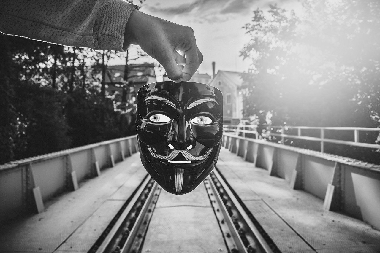 una mano tiene una maschera e sullo sfondo una strada