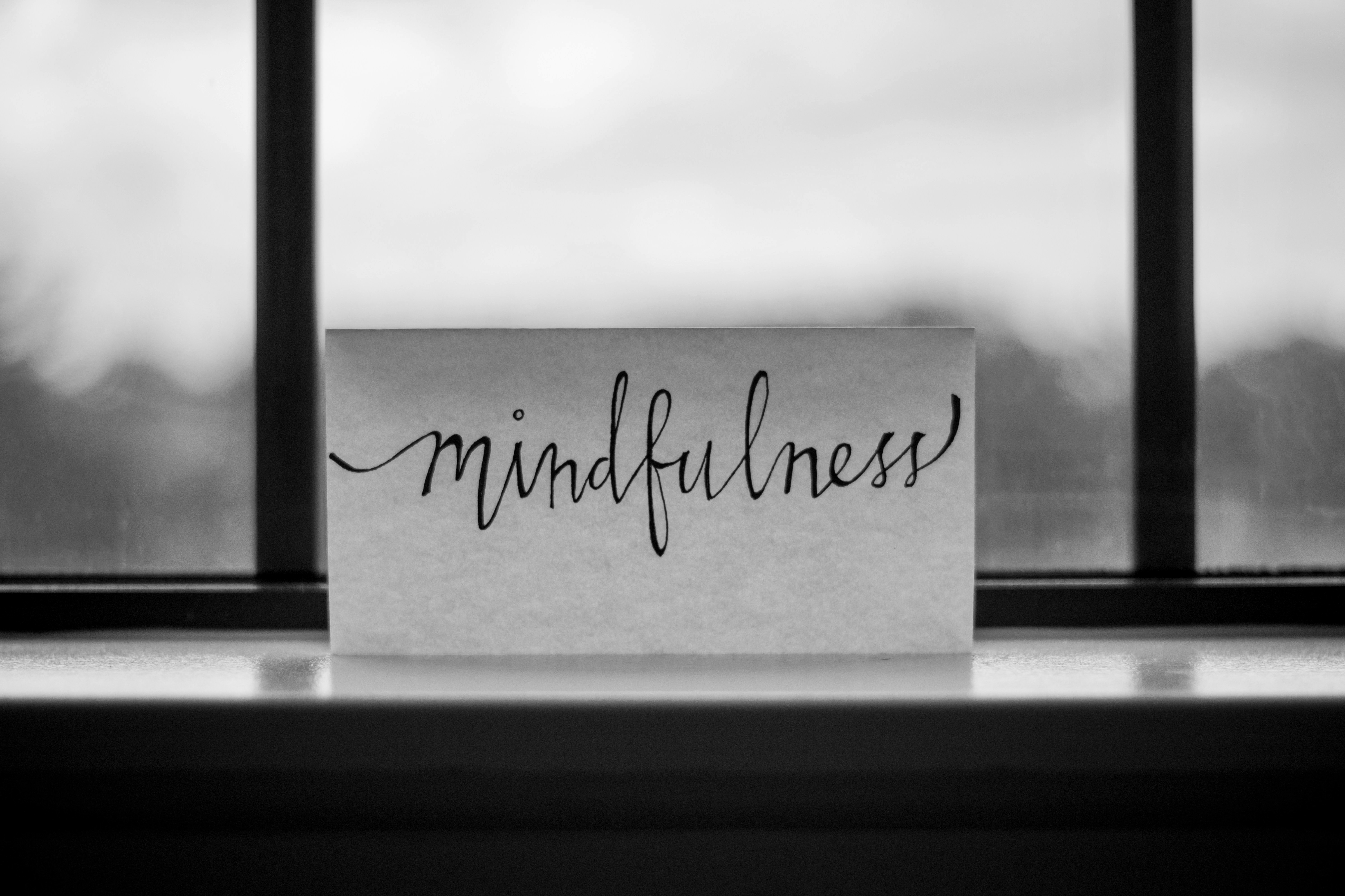 Black-and-white photo of a handwritten card reading ‘mindfulness’ placed on a windowsill